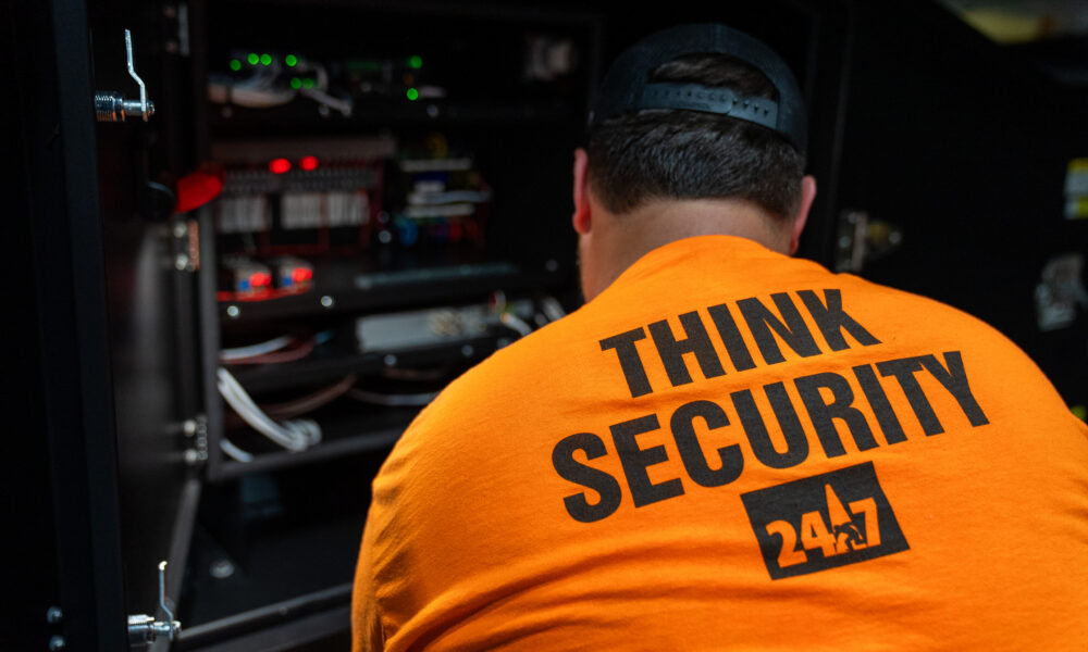 Person in orange Think Security shirt fixes electronics in cabinet.