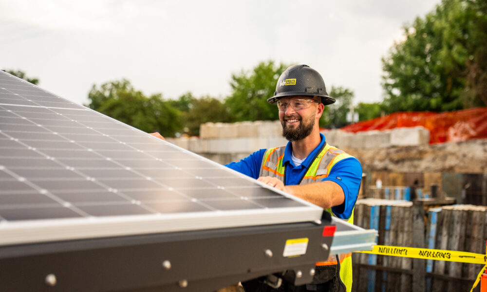 Worker in safety gear installs solar panel outdoors.