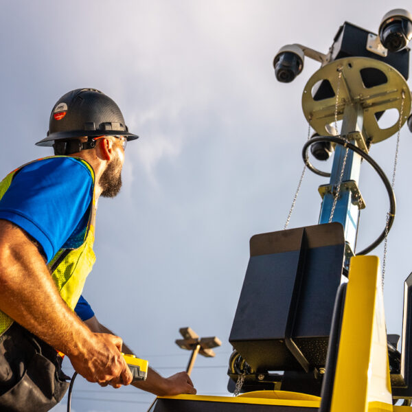 Worker at control panel by mobile camera tower, cloudy sky.