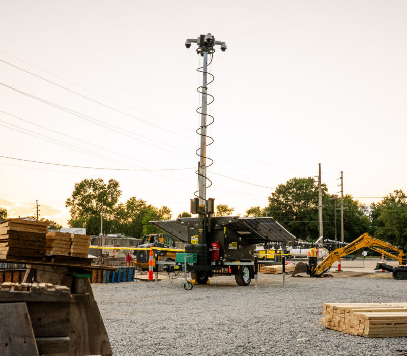 Surveillance tower with camera in construction yard at sunset.