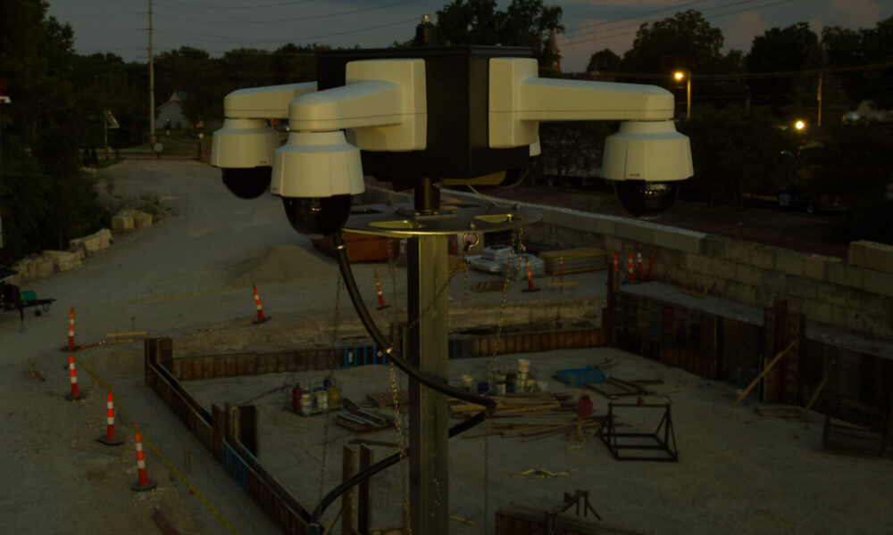 Security camera on pole oversees construction site at dusk.
