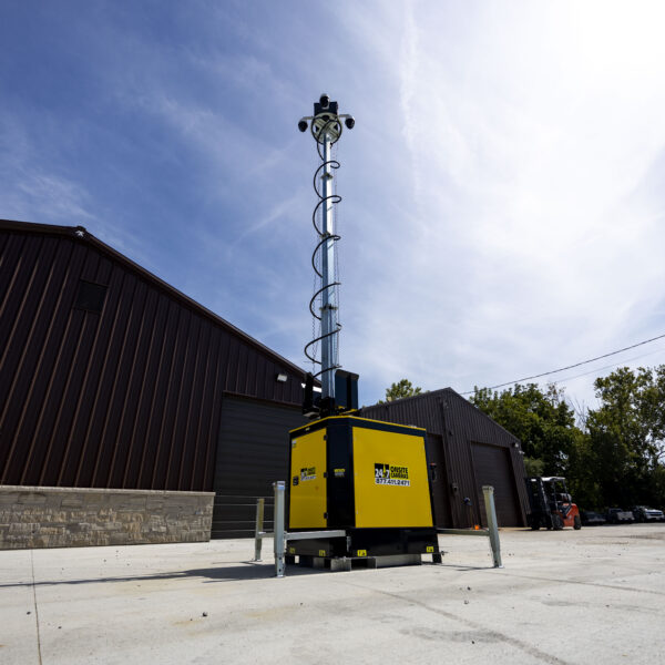 Yellow surveillance unit with camera outside brown warehouse.