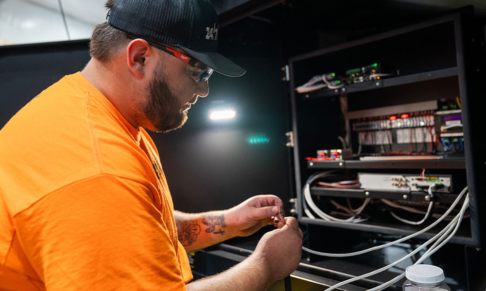 Man in orange shirt wiring inside a cabinet.