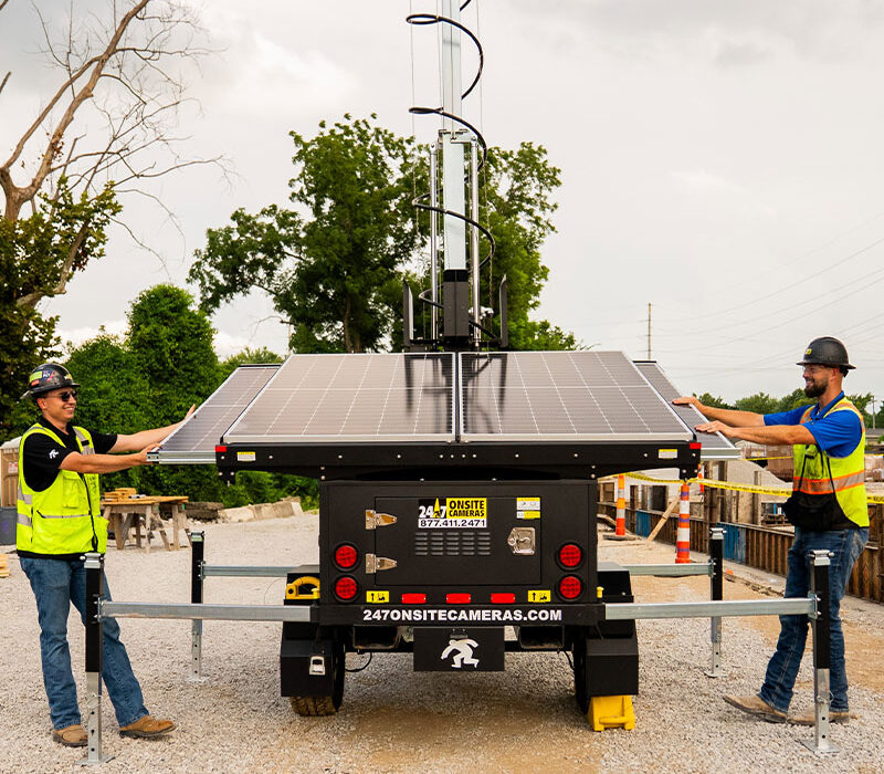 Workers adjust solar panels on a security camera at worksite.