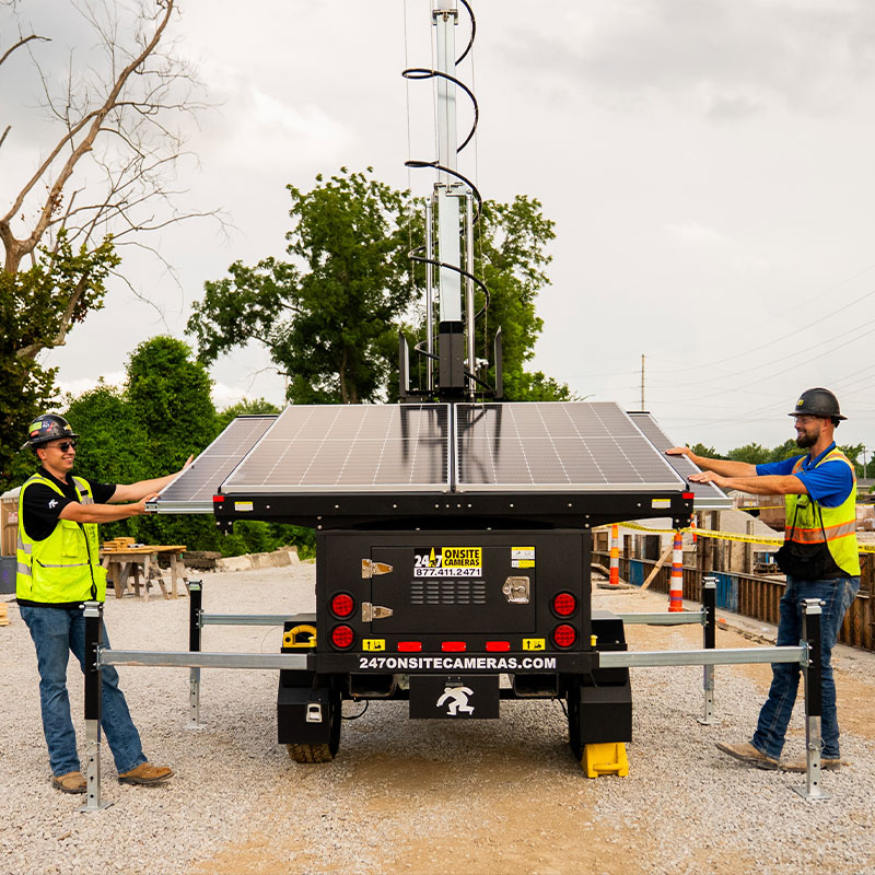 Workers adjust solar panels on a security camera at worksite.