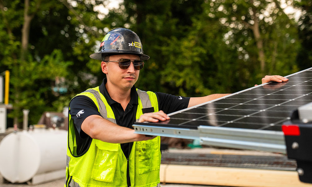 Worker in vest and helmet adjusts outdoor solar panel.