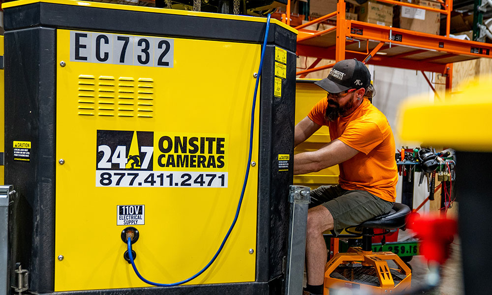 Man in orange works on yellow 24/7 security camera.