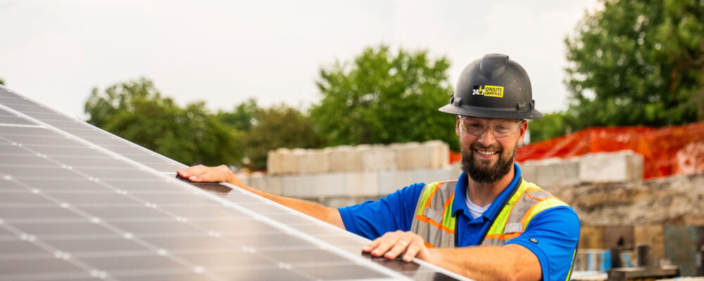Man in hard hat inspects solar panel at construction site.