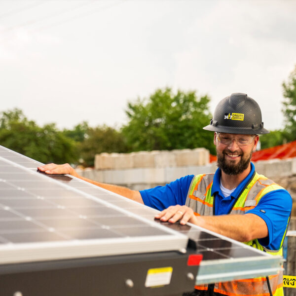 Man in hard hat inspects solar panel at construction site.
