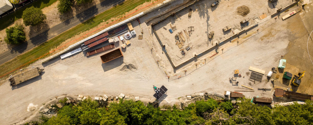 Aerial view: construction site, materials, road, vehicles, trees.