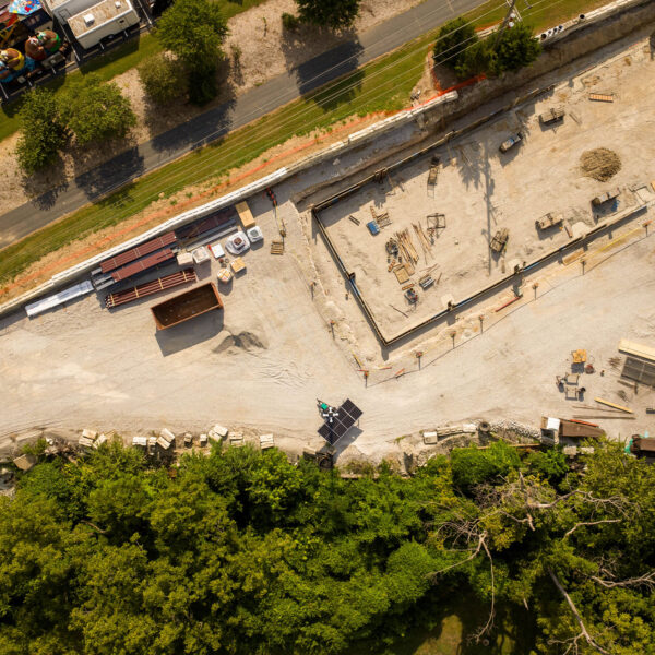 Aerial view: construction site, materials, road, vehicles, trees.