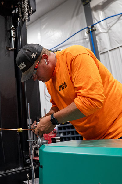 Person in orange shirt works on machinery with tools.