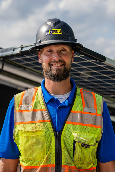 Smiling man in hard hat by solar panels outdoors.