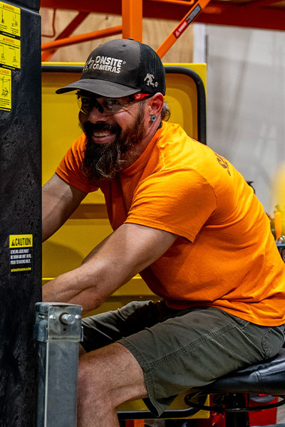 Man in orange shirt operates indoor machinery with warning labels.