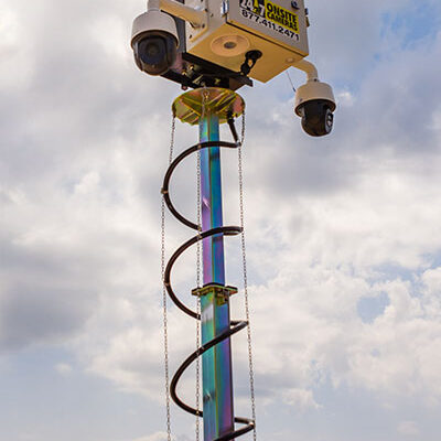Surveillance camera on spiral pole, cloudy sky and trees.