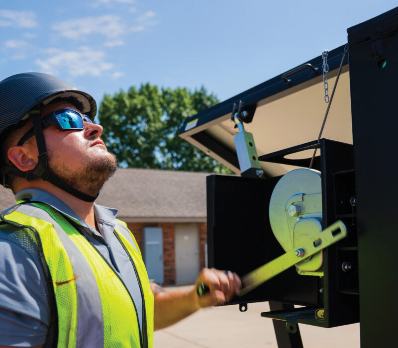 Worker in safety gear uses hand winch outdoors.