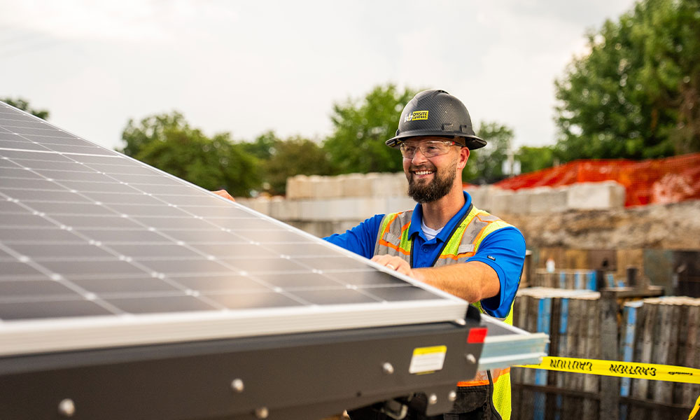 Worker in safety gear installs solar panel outdoors.