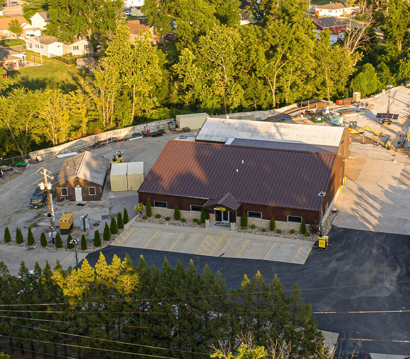 Aerial view: brown-roofed building, parking lot, trees.