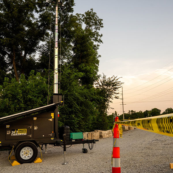 Security camera tower on gravel road by cones and tape.