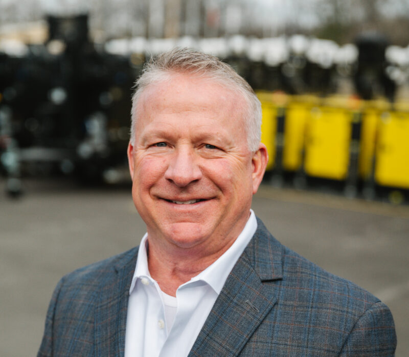 Smiling man in checked suit outdoors near industrial equipment.