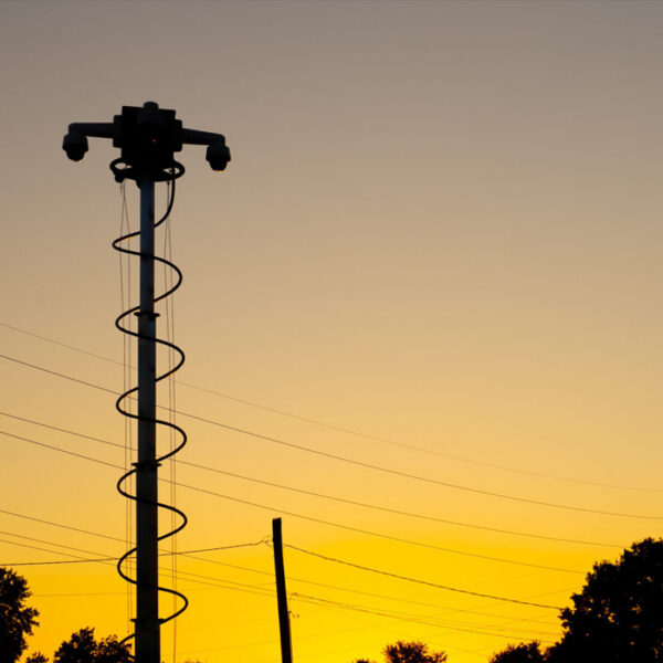 Silhouetted security camera tower at sunset with trees nearby.